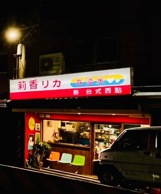 莉香リカ在淡水店舖外觀夜景，紅底招牌寫著「莉香リカ在淡水・新台式西點」，位於淡水淡金路四段546號之1、聖約翰科技大學正對面